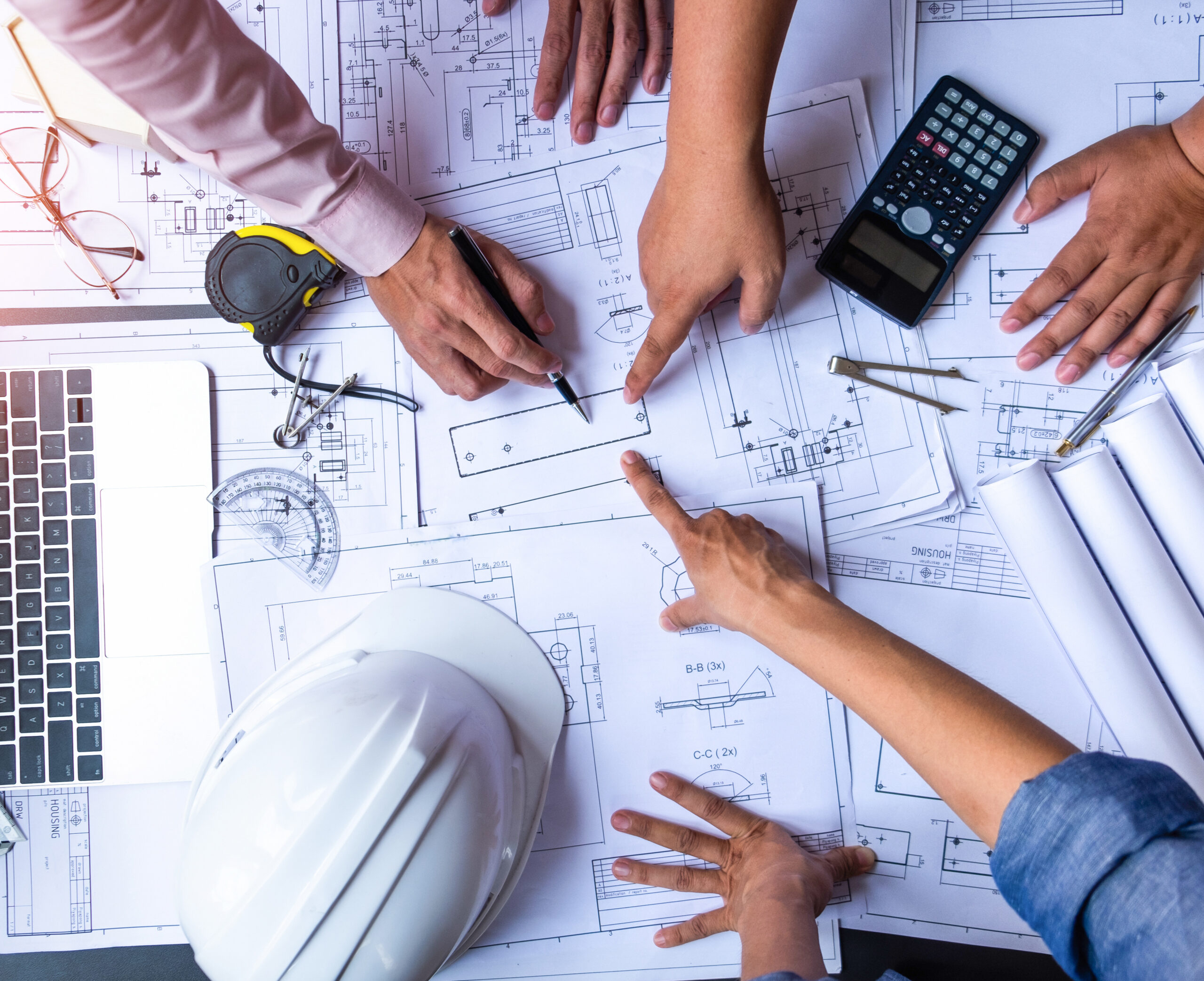 engineers pointing to building on blueprint and using laptop to